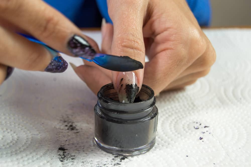 Acrylic dip powder being dropped on top of a finger nail