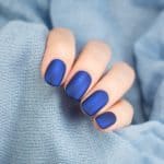 Beautiful blue matt manicure. Blue background closeup.