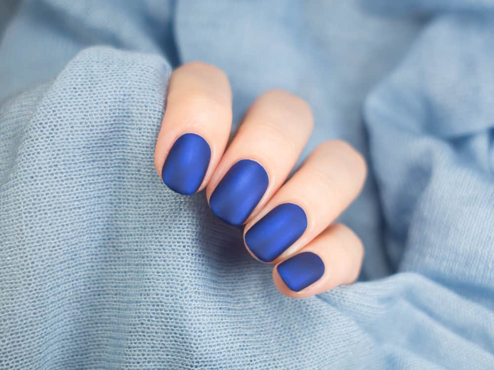 Beautiful blue matt manicure. Blue background closeup.