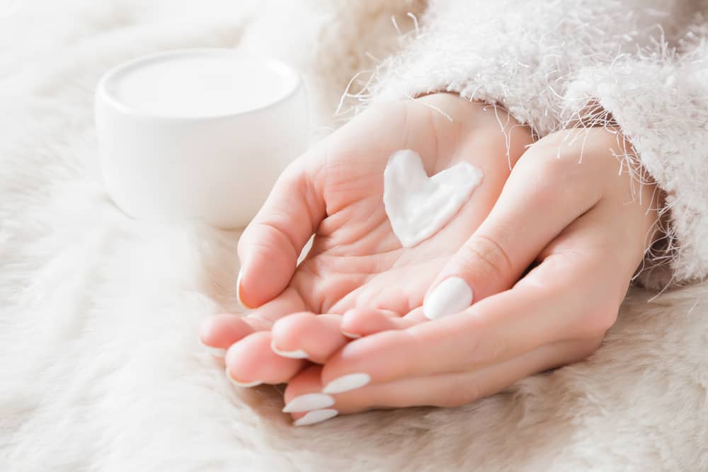 Beautiful groomed woman's hands with cream jar on the fluffy blanke