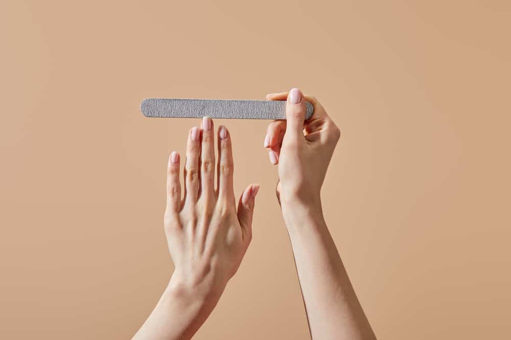 Cropped view of woman filing nail with emery board