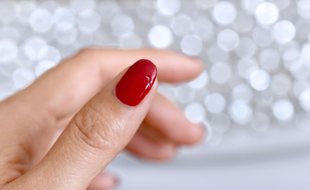 Damaged female thumb nail with red manicure