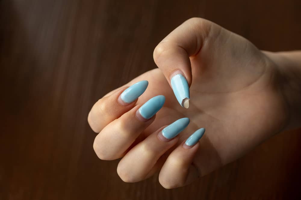 Damaged nail polish of blue color on regrowth nails of the hand