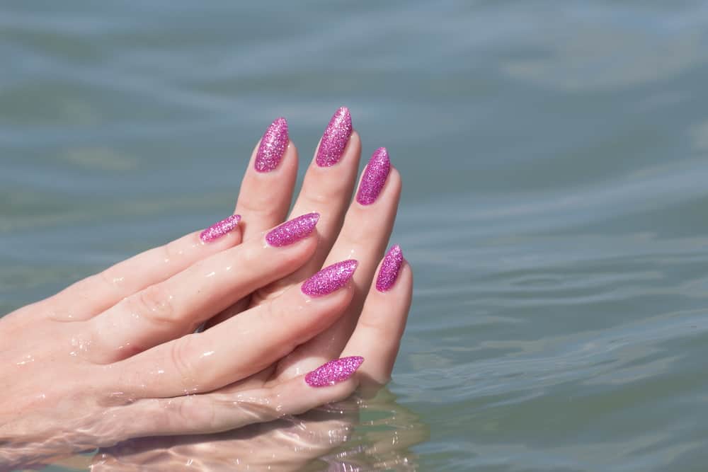 Female hands with pink nails in sea water