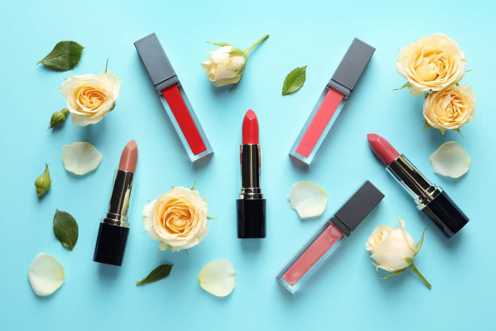 Flat lay composition with lipsticks and roses on color background