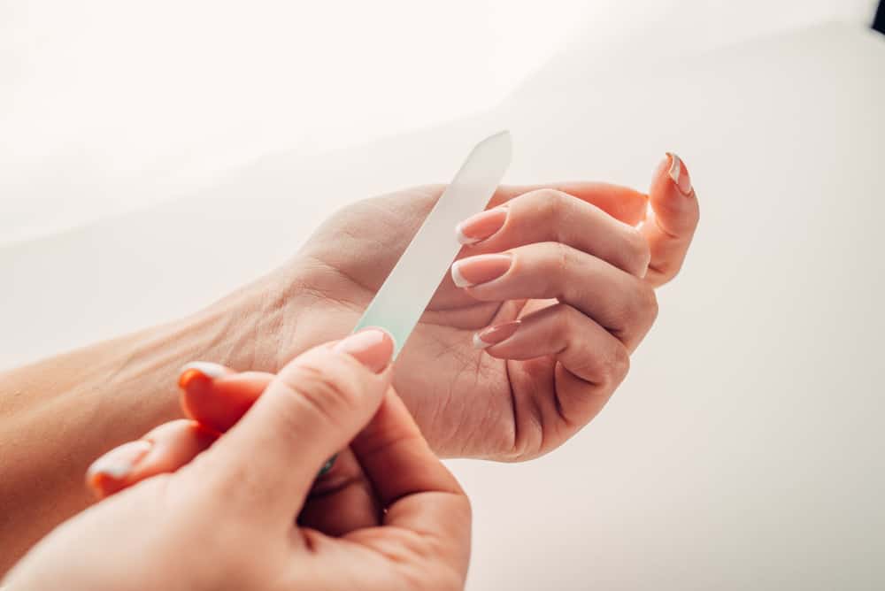 Hand filing nails with glass nail file on the white background