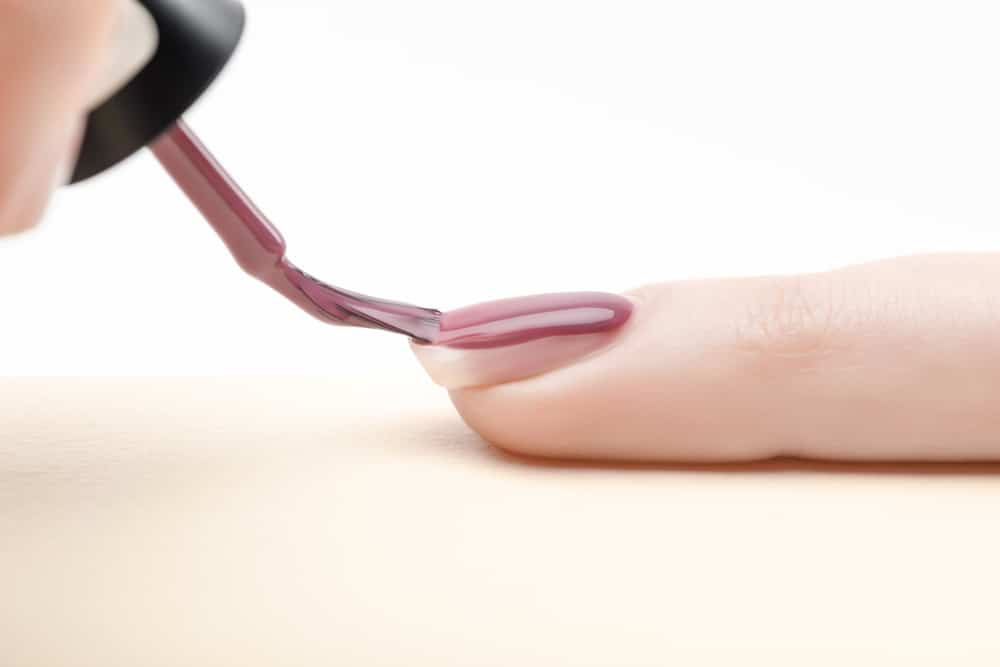 Manicurist applying purple nail polish on fingernail of woman