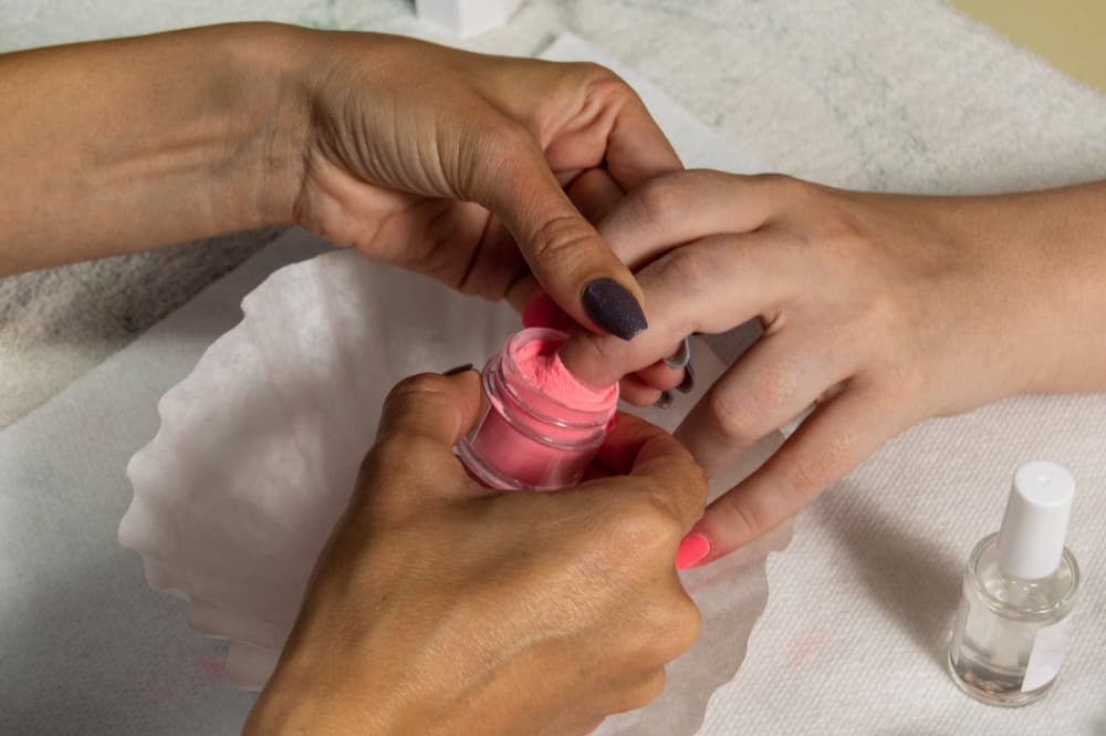 Manicurist using dip powder to give a girl a manicure