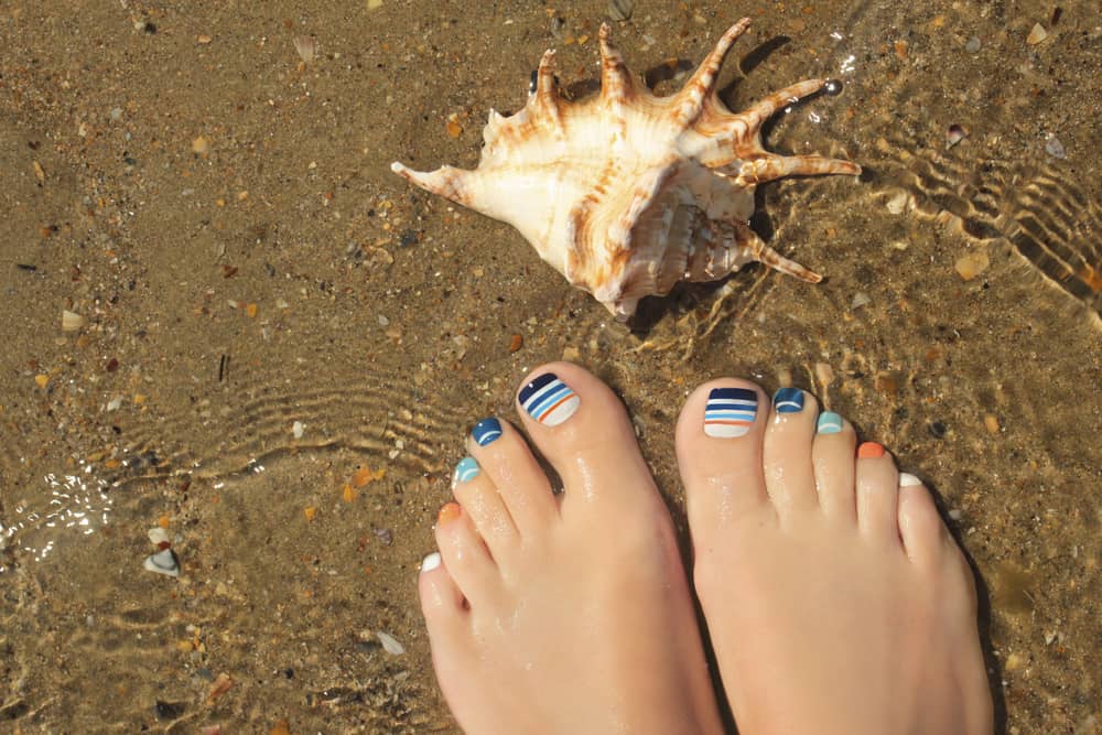 Marine striped multicolored pedicure on female nails on summer sea closeup