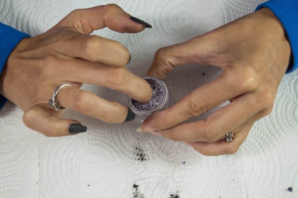 Middle finger of a Caucasian hand being dipped in sparkly dip powder