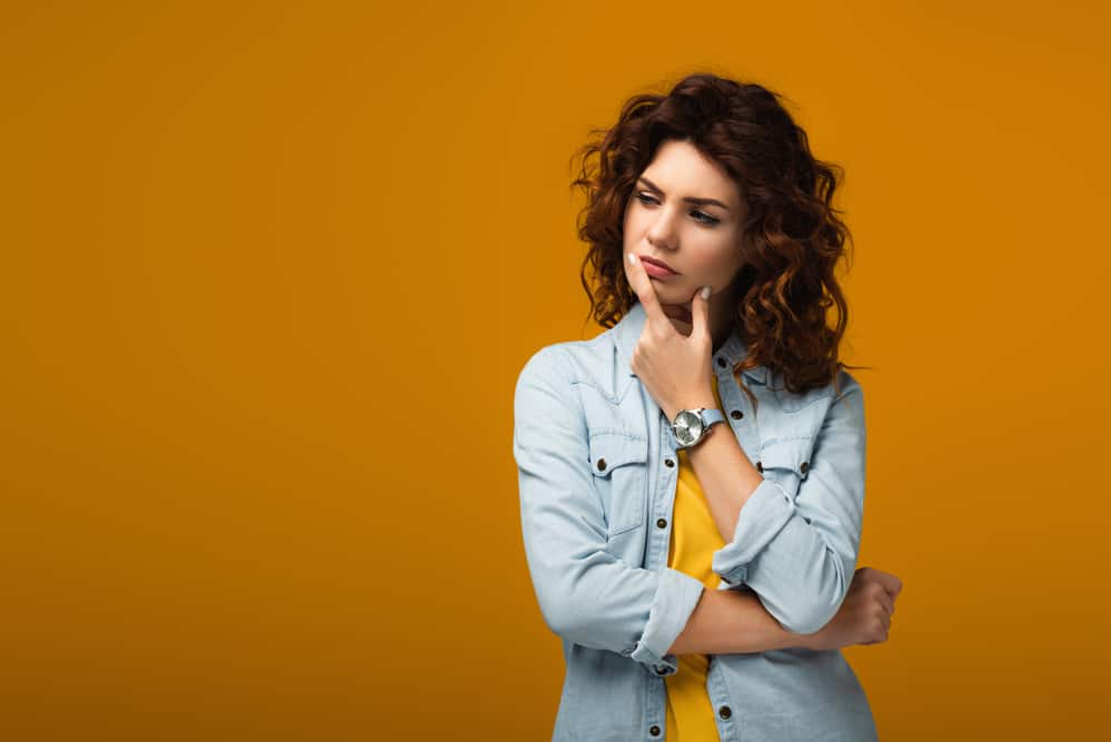 Pensive curly redhead woman touching lips while thinking