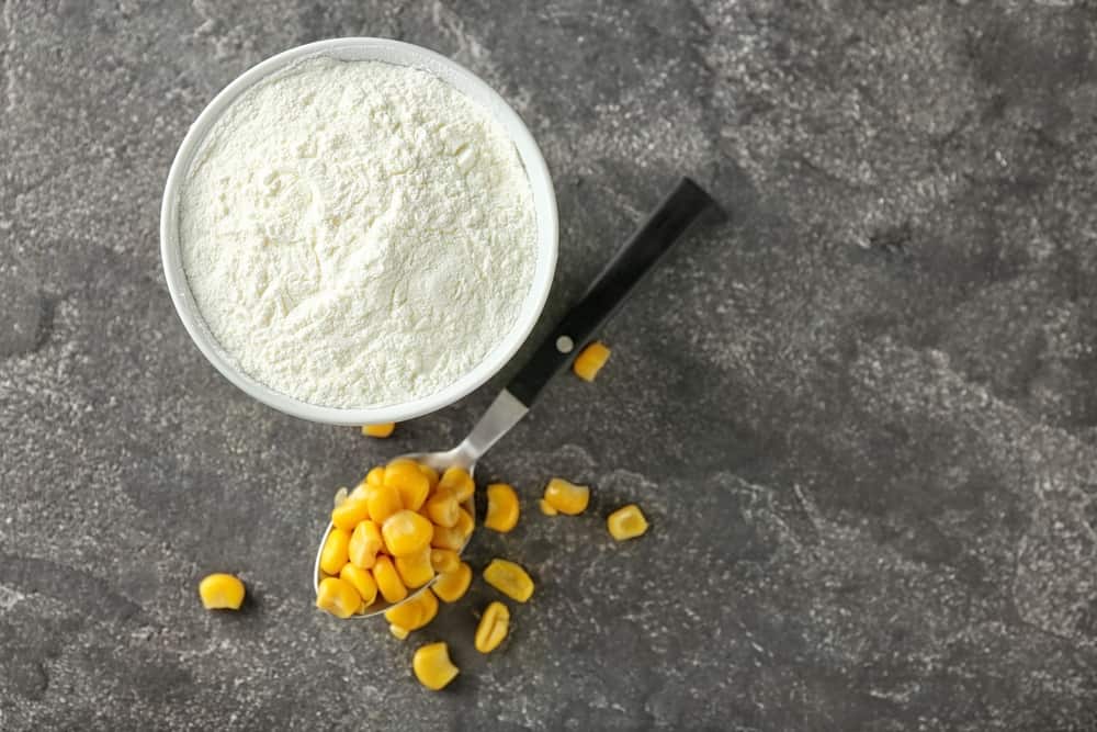 Spoon with kernels and corn starch in bowl on table