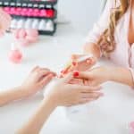 Woman in salon receiving manicure by nail beautician