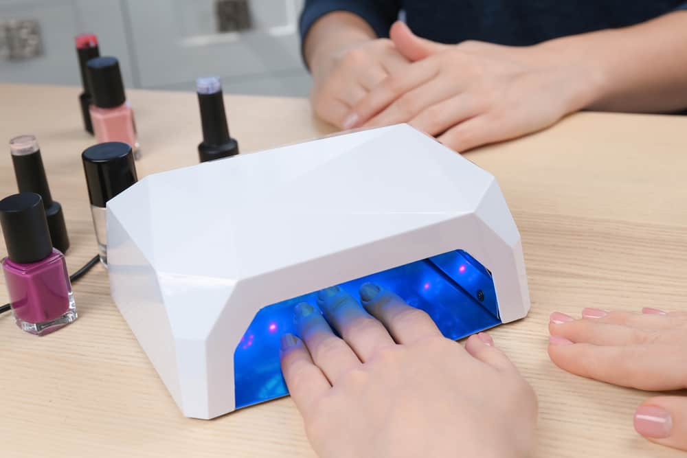 Woman using UV lamp for manicure at table