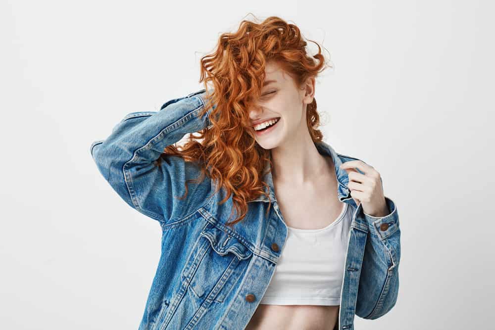 girl smiling with closed eyes touching her red curly hair