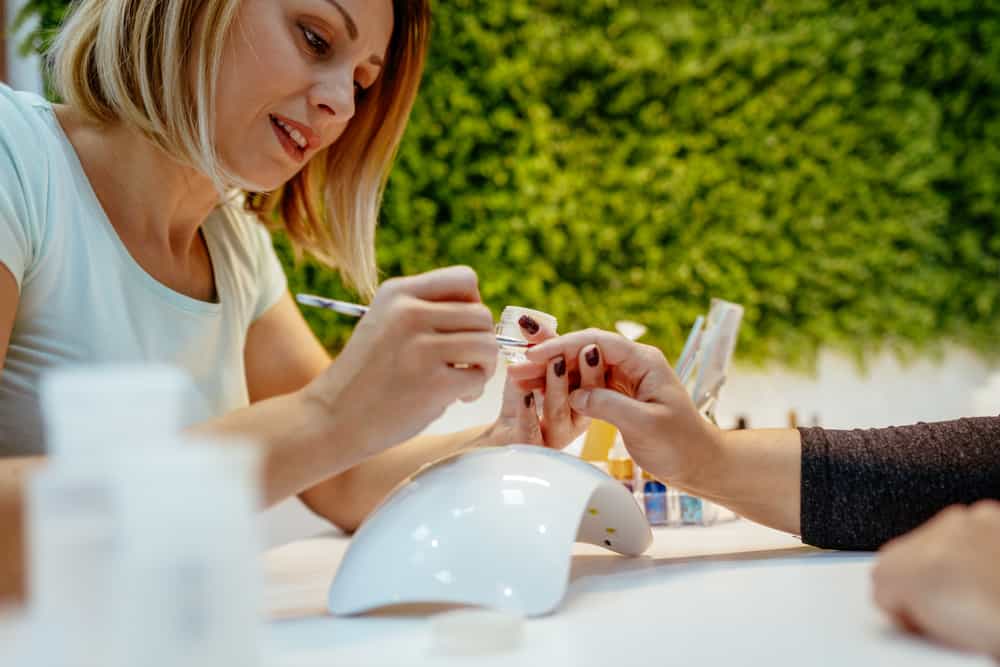 Beautician polishing female nails with nail file in beauty salon