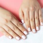 Beautiful women's hands with white manicure on a pink and white background