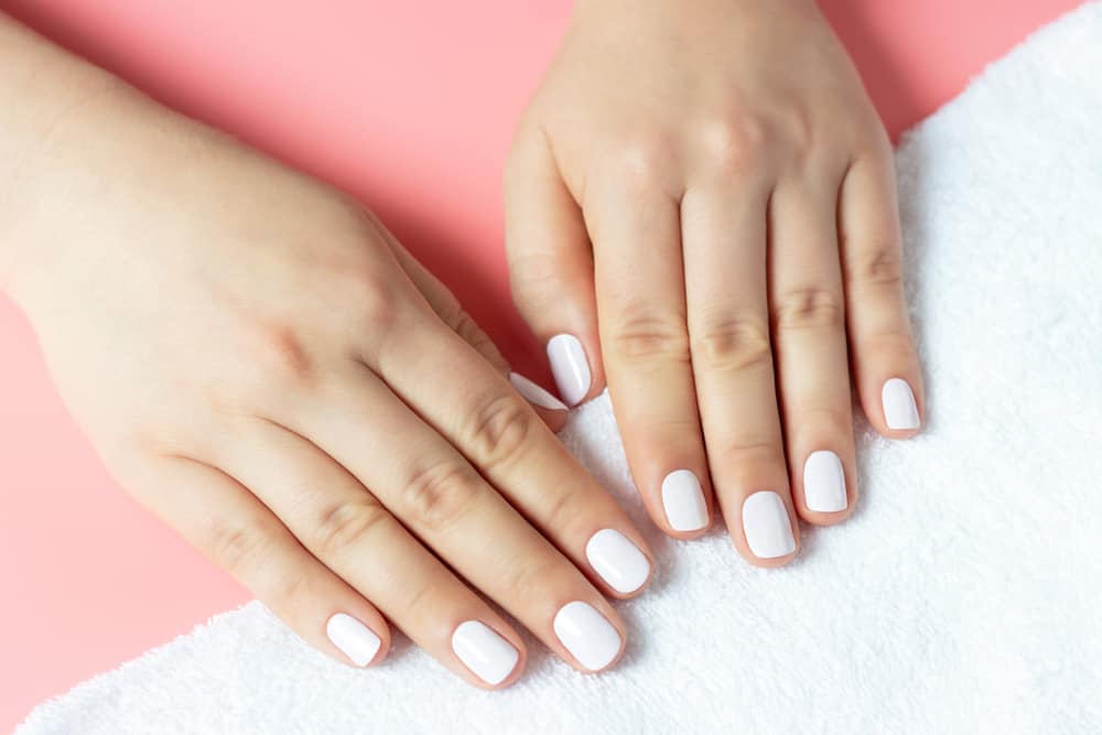 Beautiful women's hands with white manicure on a pink and white background