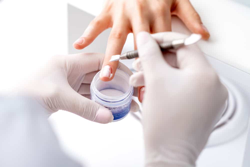 Close up of the process of applying acrylic powder on the nails of a young woman in a beauty salon