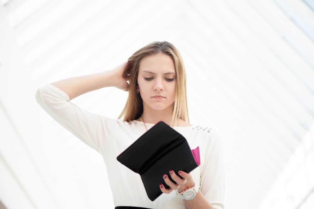 Upset young woman out of money looking into opened wallet in shock, tight budget, broke