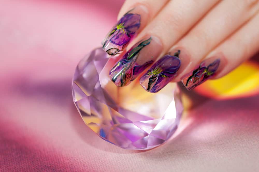 Fingers with beautiful manicure touch a shining diamond