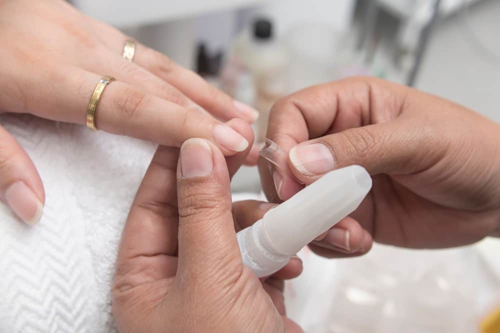 A manicurist places a clear nail extension form to the finger