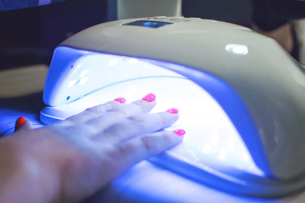 Female Hand with red nails in the lamp for manicure