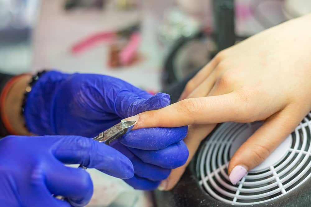 Manicurist with blue gloves rasping nails on women's hand