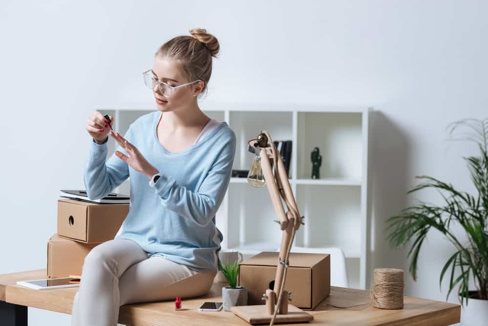 Portrait of young woman applying nail polish while sitting