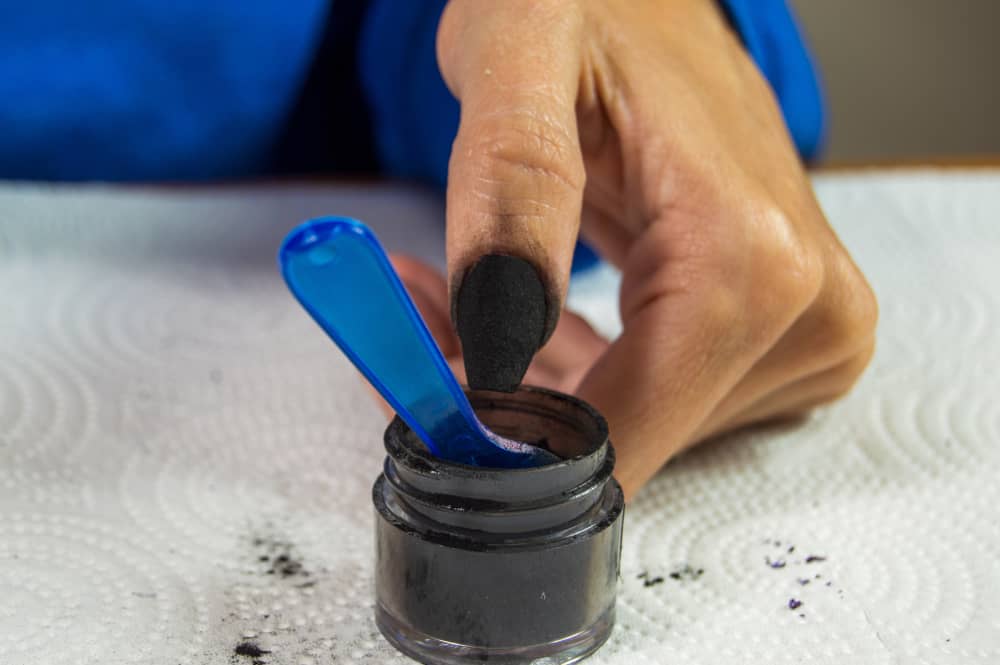 Woman dipping left thumb in black dip powder