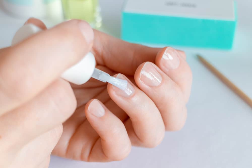 Woman doing at-home manicure, applying nail conditioner or base coat