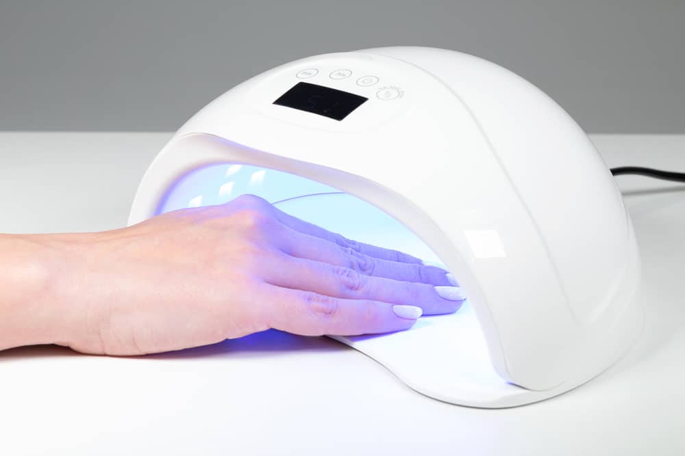 Woman puts hand into led uv lamp for curing