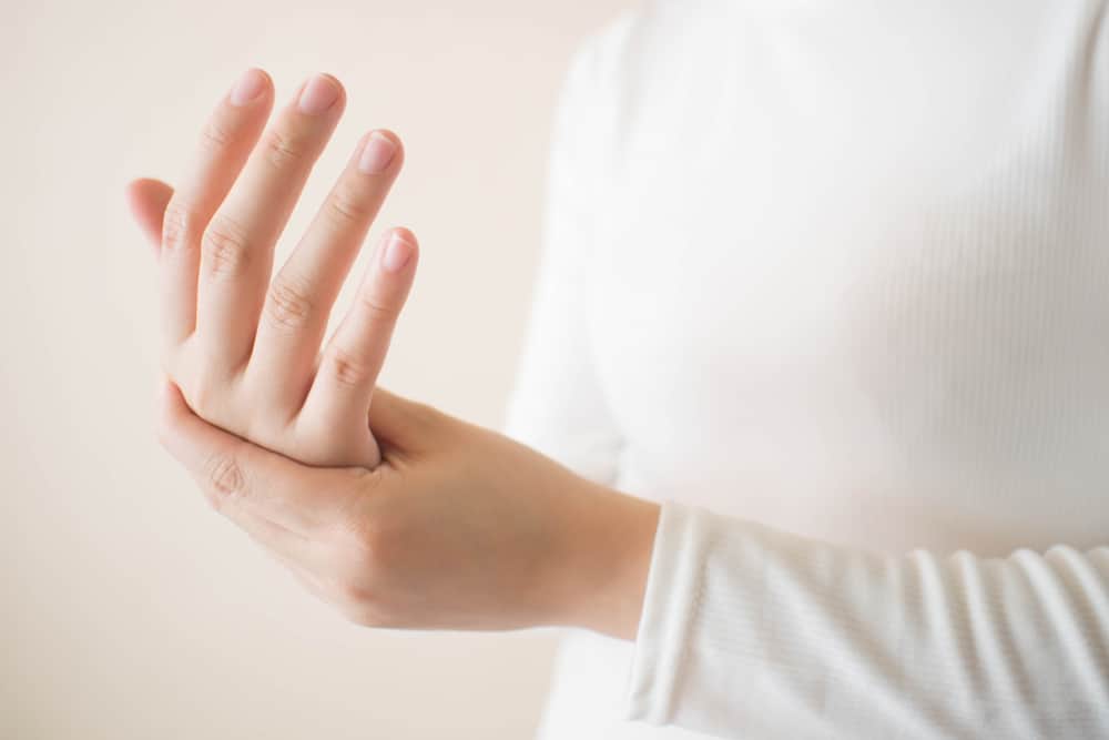 Young female in white t-shirt suffering from pain in hands and massaging her painful hands