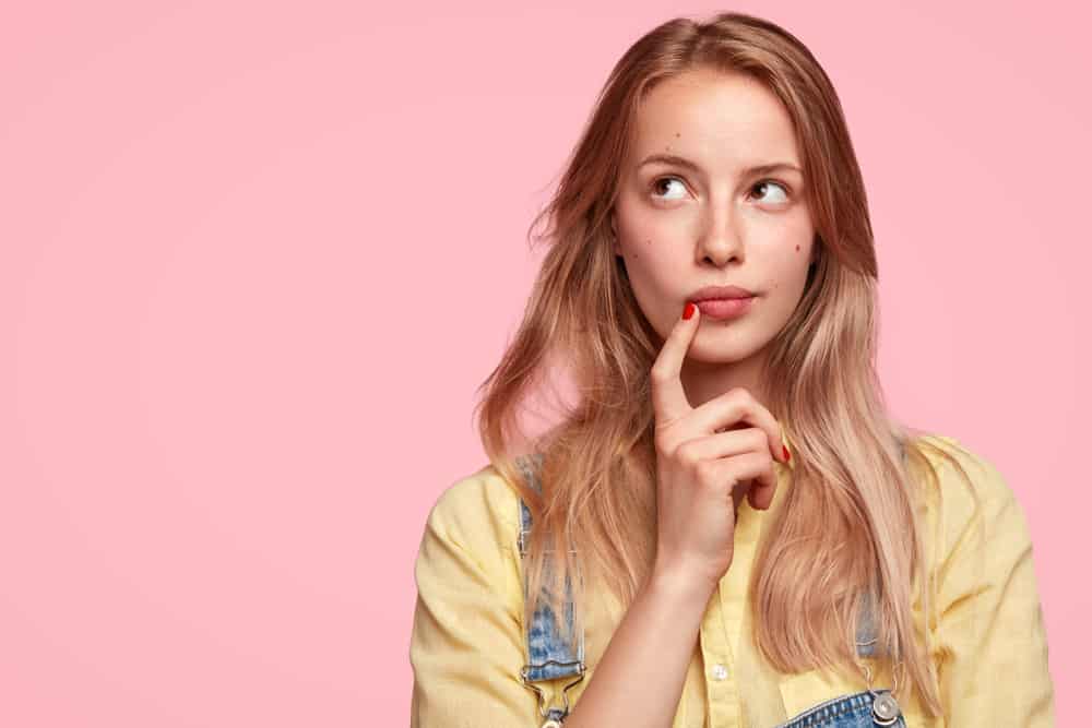 female youngster keeps fore finger near lips thinking