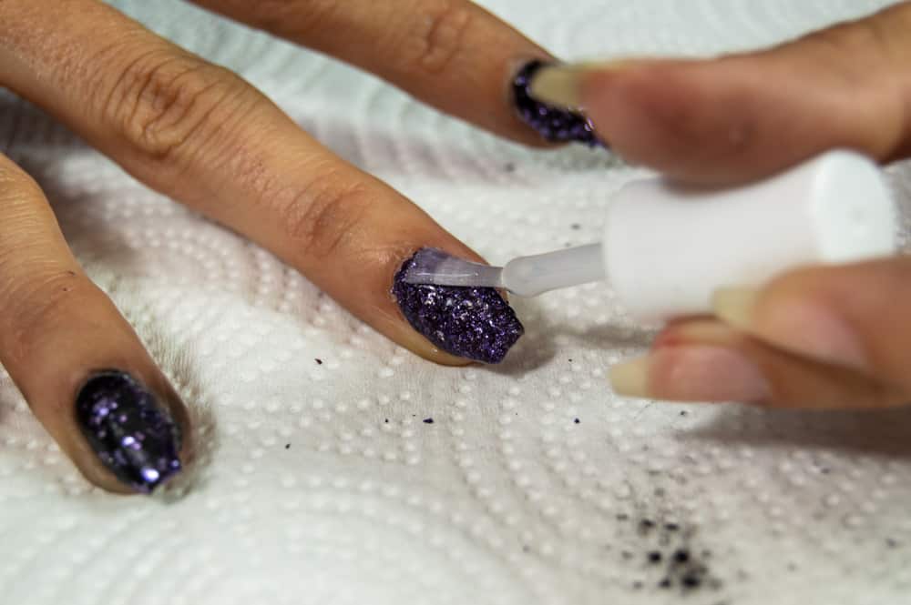 top coat of clear nail polish being applied to a beautiful sparkling fingernail